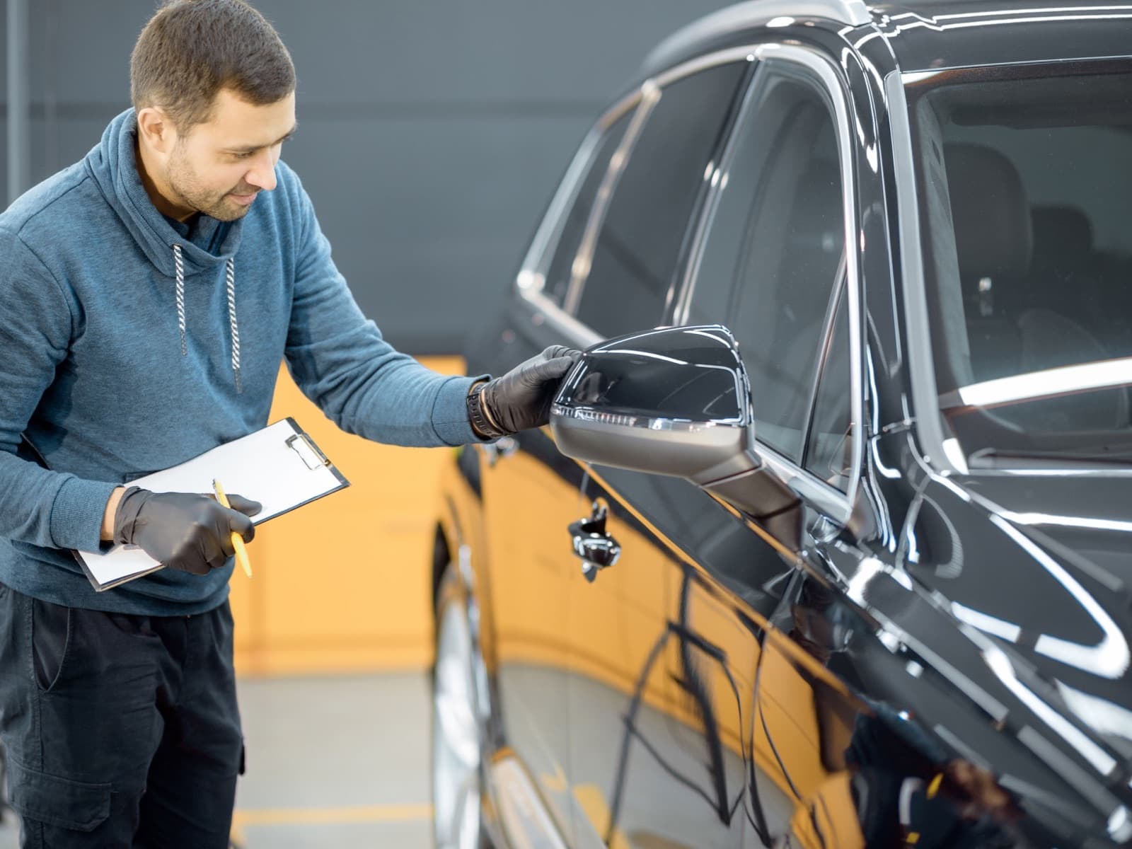 Man inspecting shiny black car at workshop.