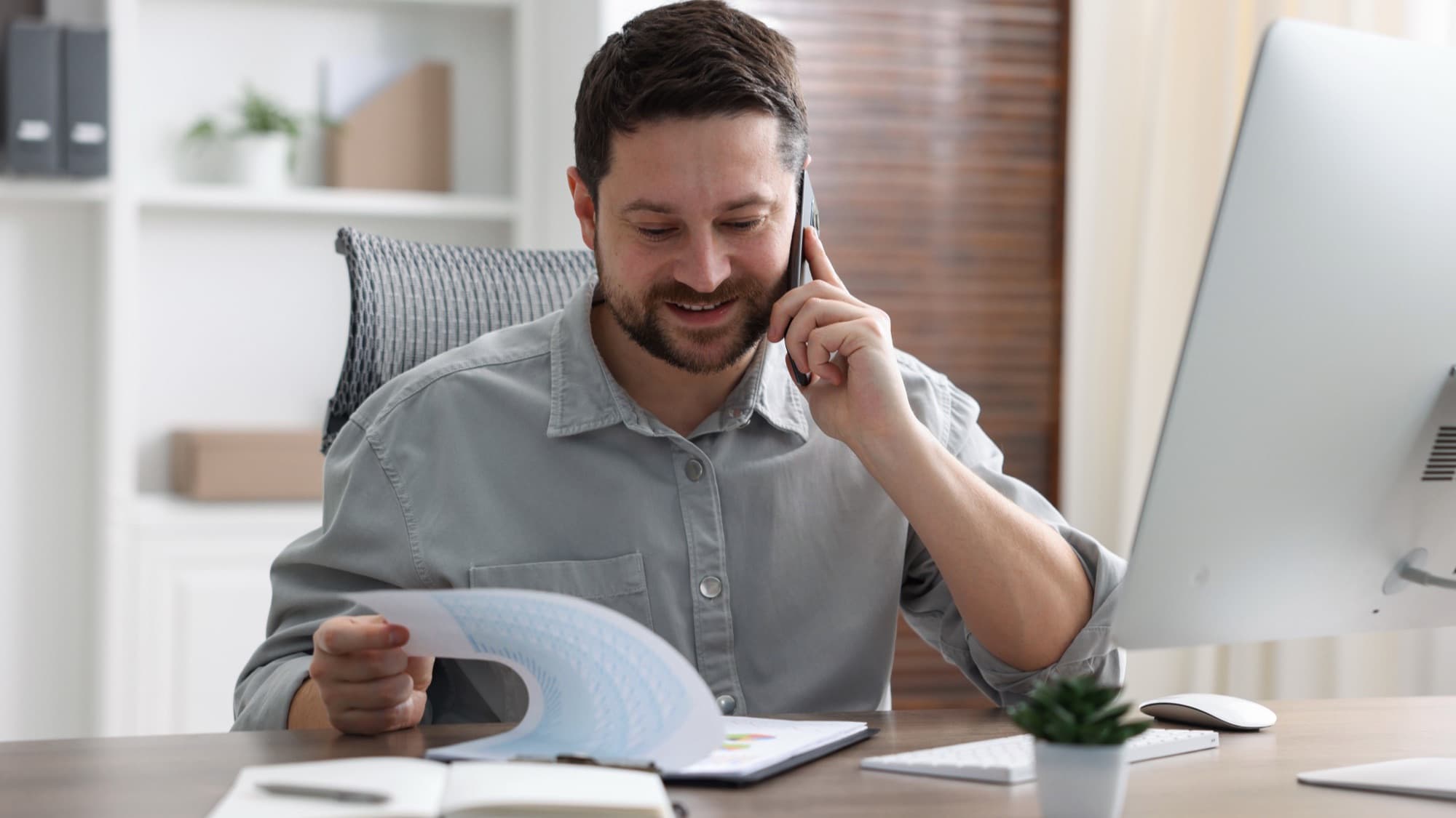 Focused businessman talking on phone while reviewi.
