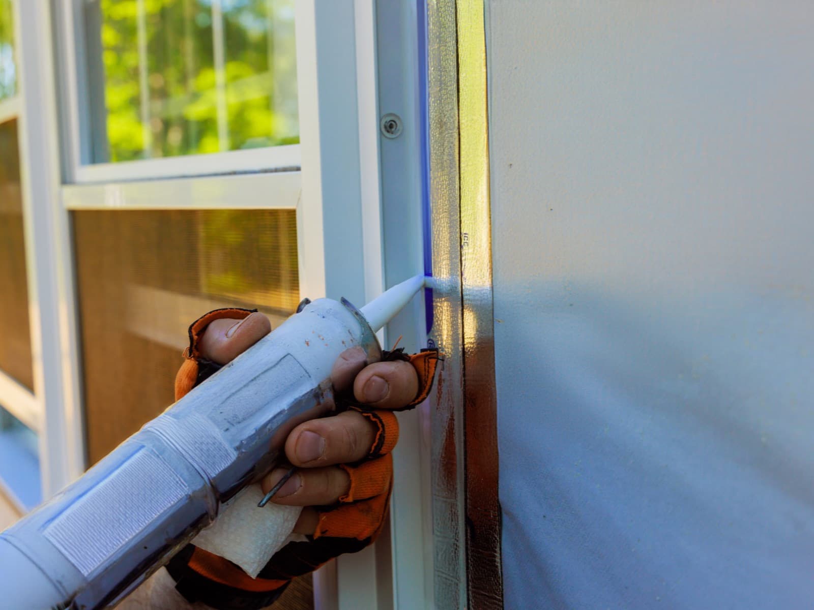 Caulking gun applying sealant near a window.