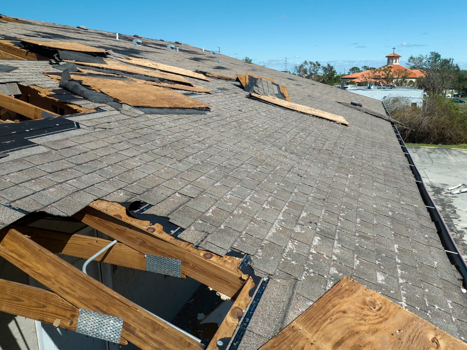 Damaged roof with missing shingles on sunny day.