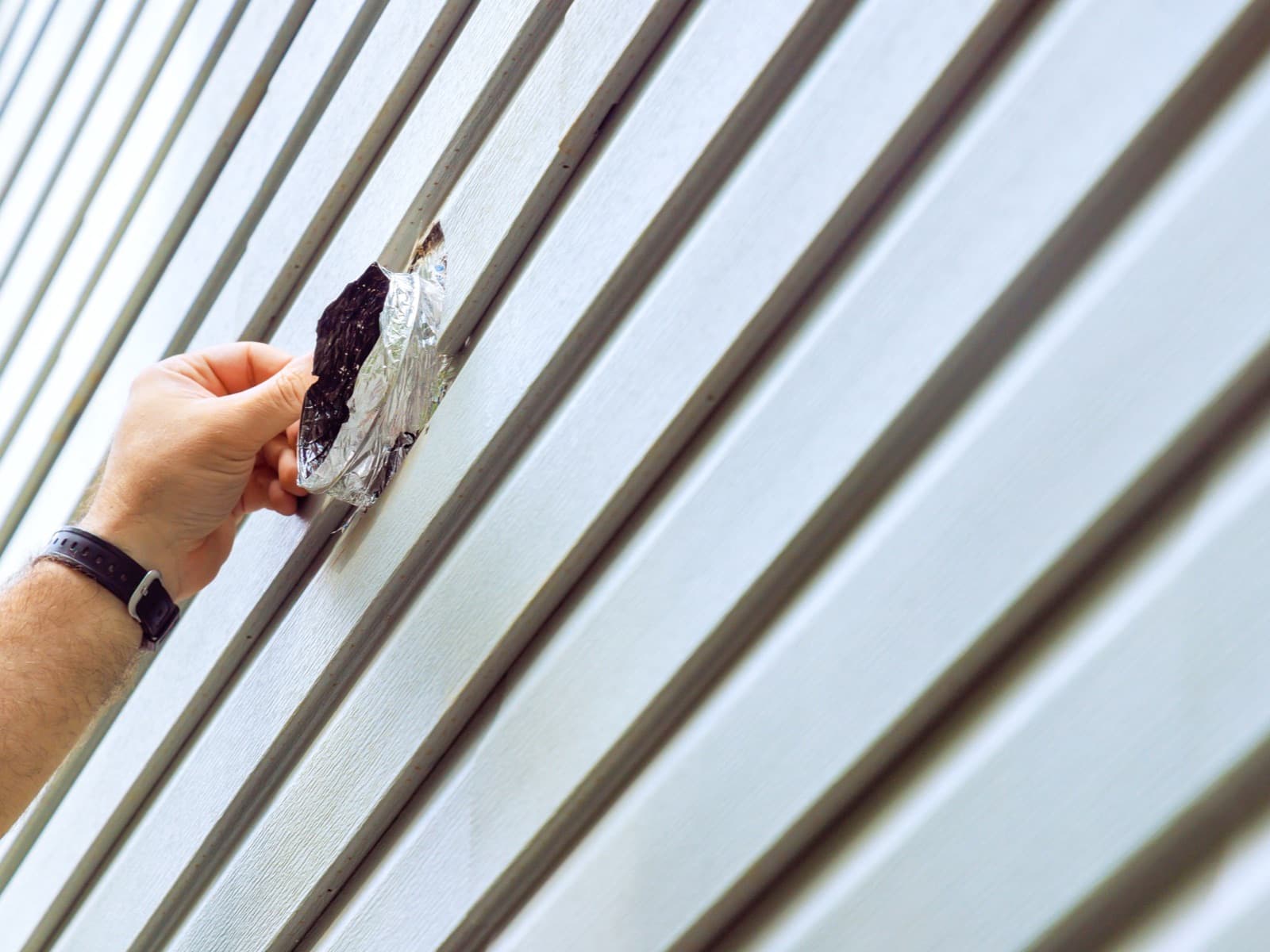 Hand repairing damaged exterior wall siding panel.